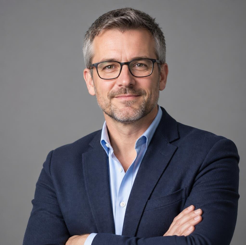 Studio headshot of a British male broadcast instructor wearing glasses