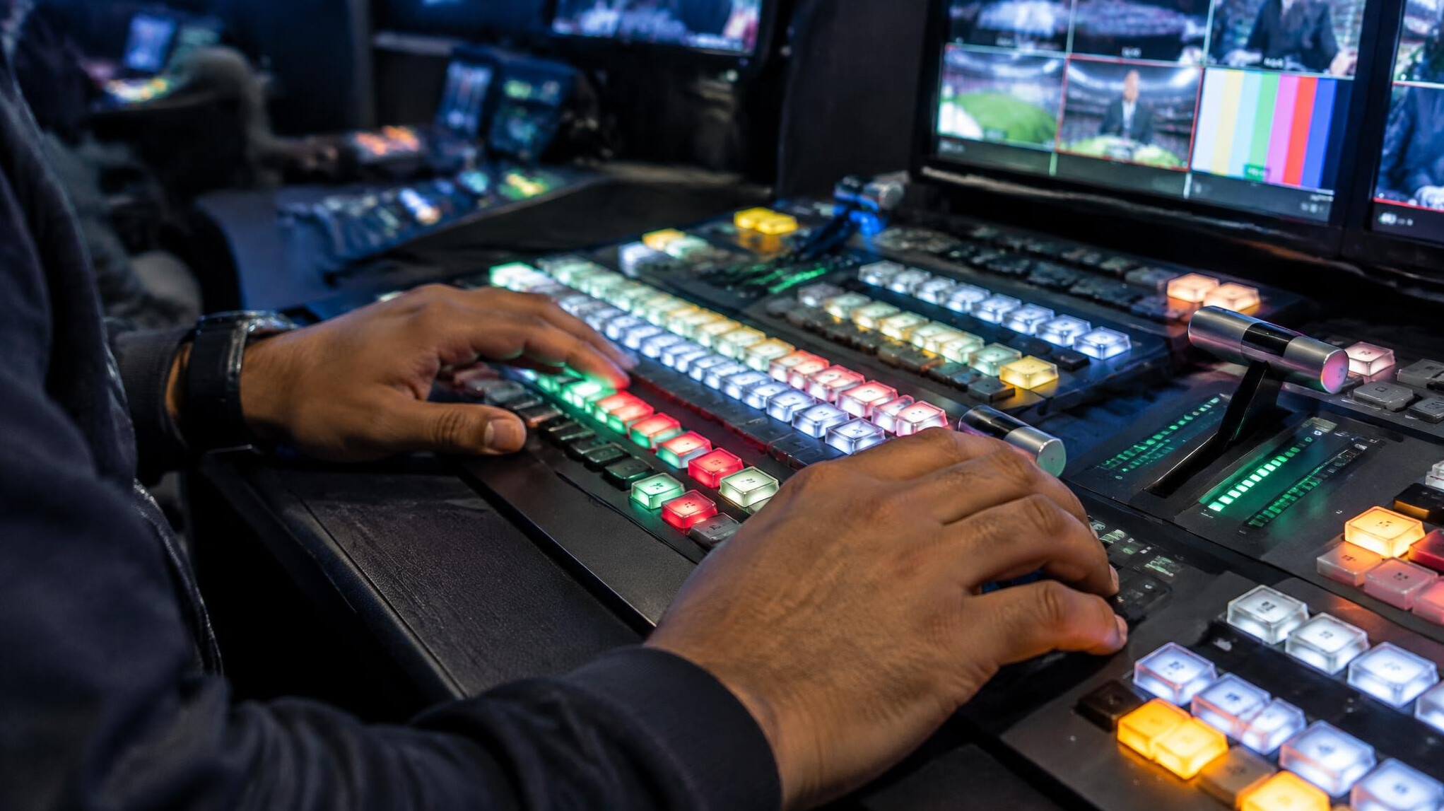 Close-up of hands operating a professional video switcher panel with illuminated buttons